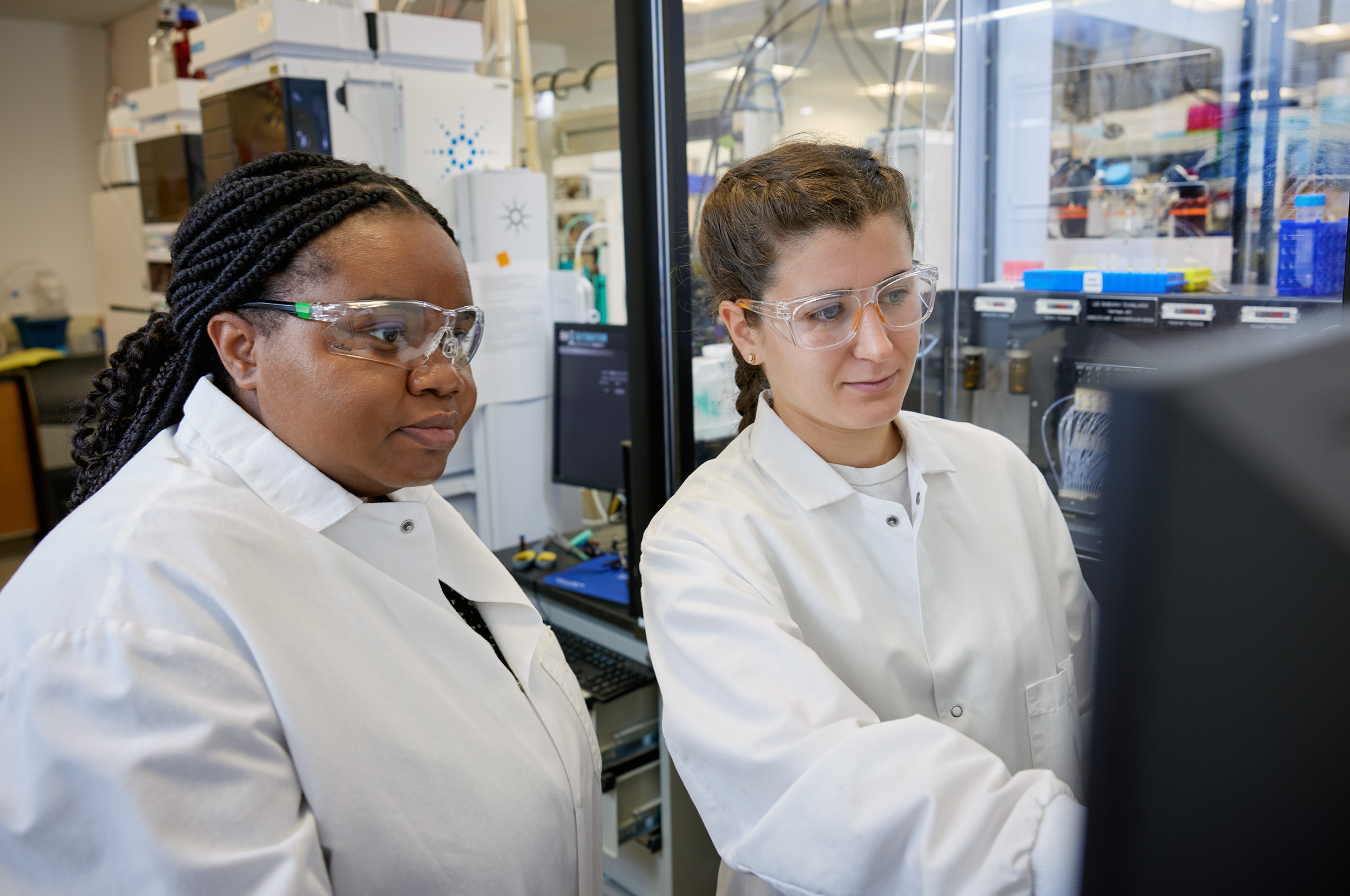 Two women in lab coats looking at a computer screen.