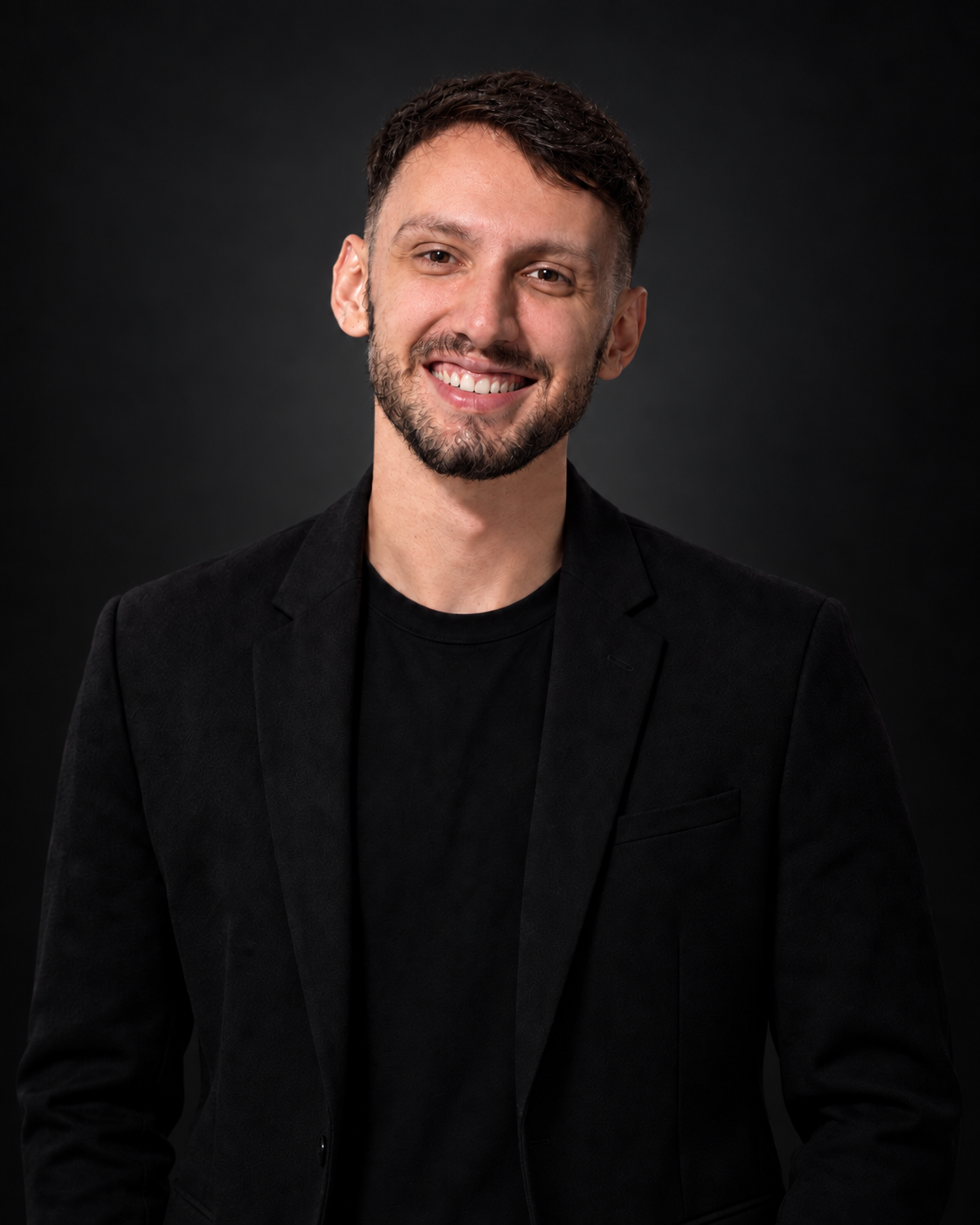 Retrato de Airton Tassin em fundo escuro, usando blazer preto.