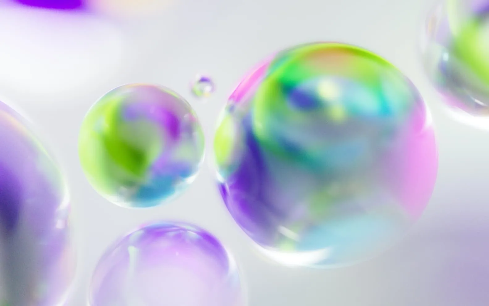 Close-up of translucent bubbles with swirling green, purple, and blue colors on a light background.
