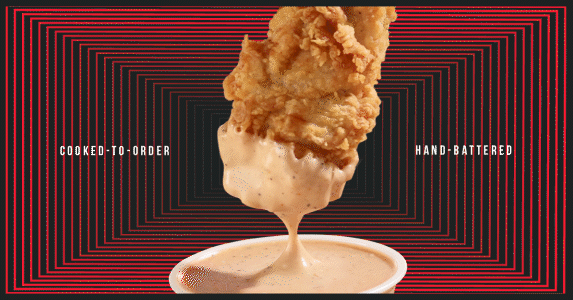 A chicken wing is being dipped into a cup of sauce.