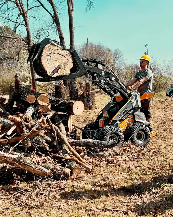 Tree service worker using a Giant mini skid steer to remove large logs during land clearing in Tulsa, part of Hickman Trees’ professional tree removal services
