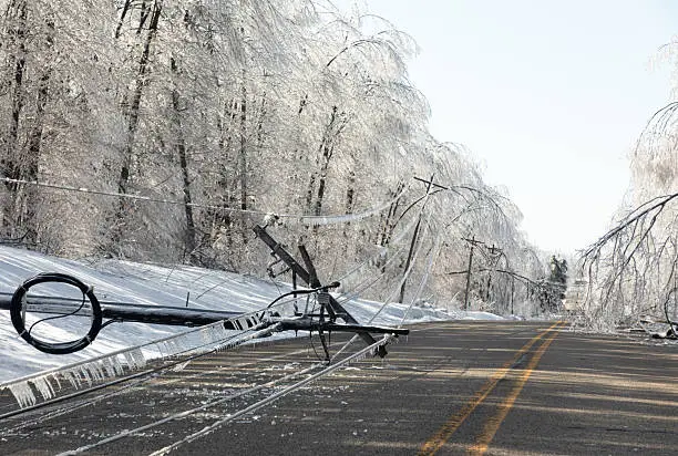Ice-covered trees and downed power lines blocking a road after a winter storm, illustrating serious tree hazards Tulsa homeowners may face.