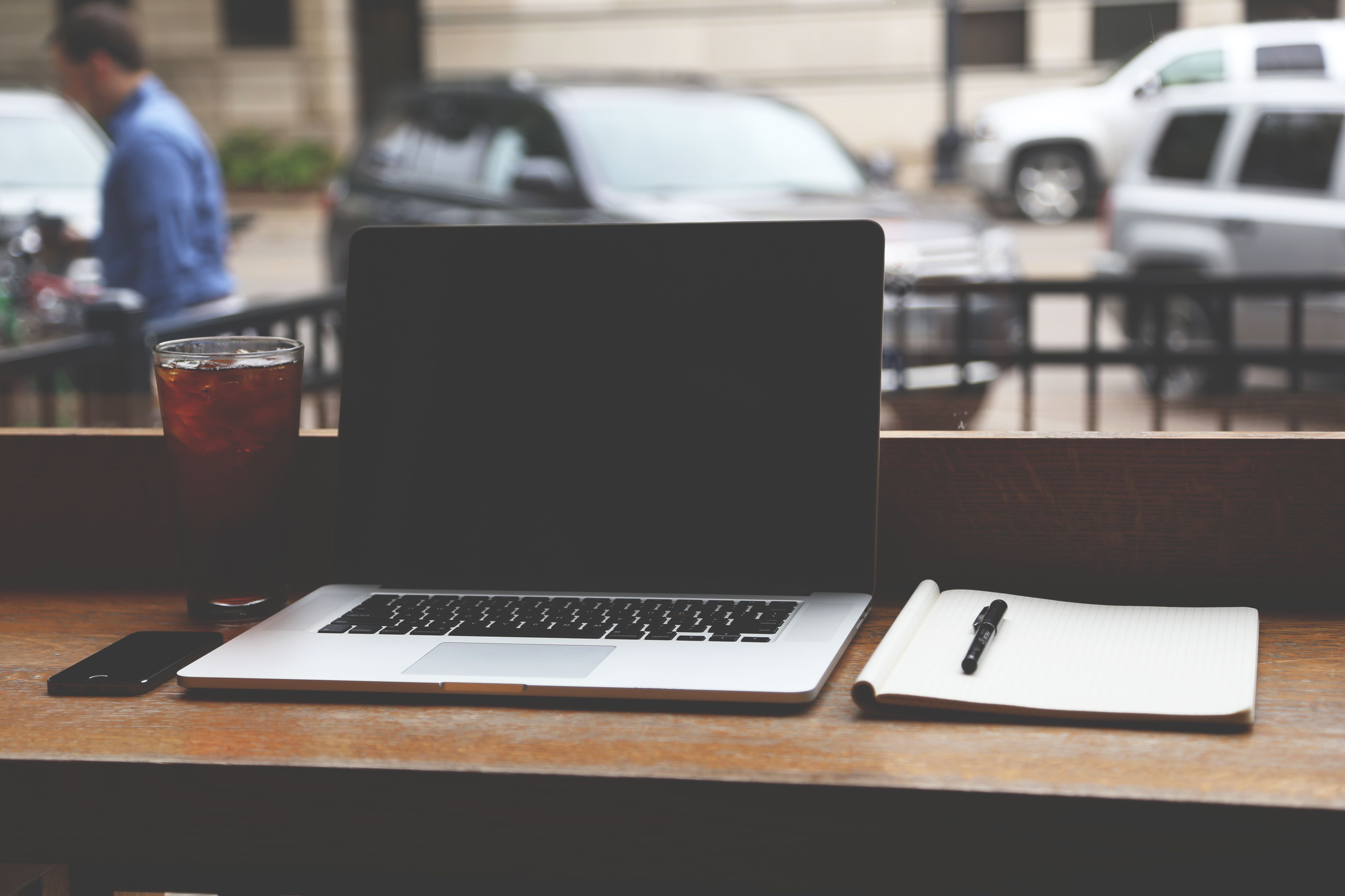 A laptop, notebook and pen on a wooden counter in a cafe