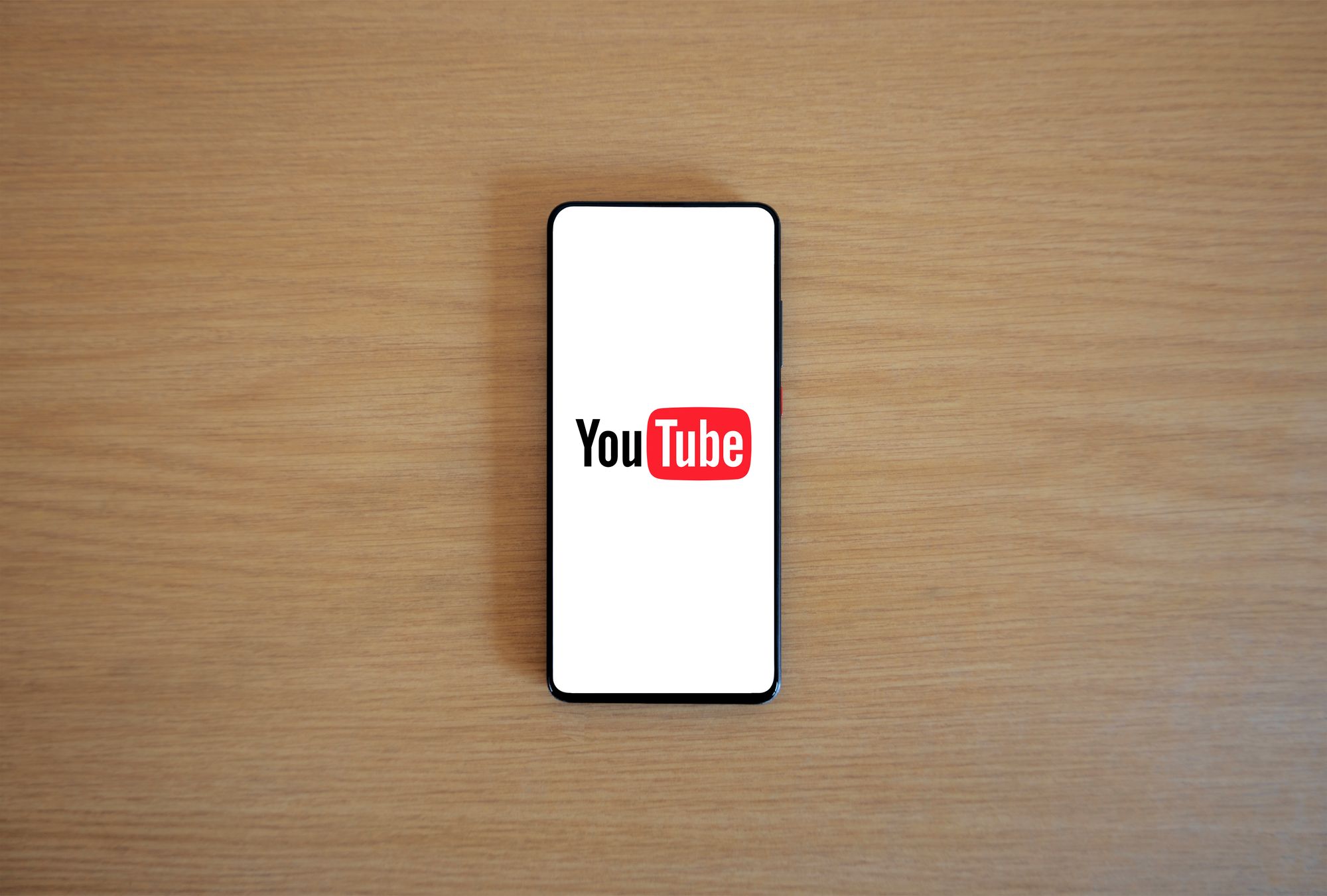 A phone showing the YouTube logo on a wooden desk