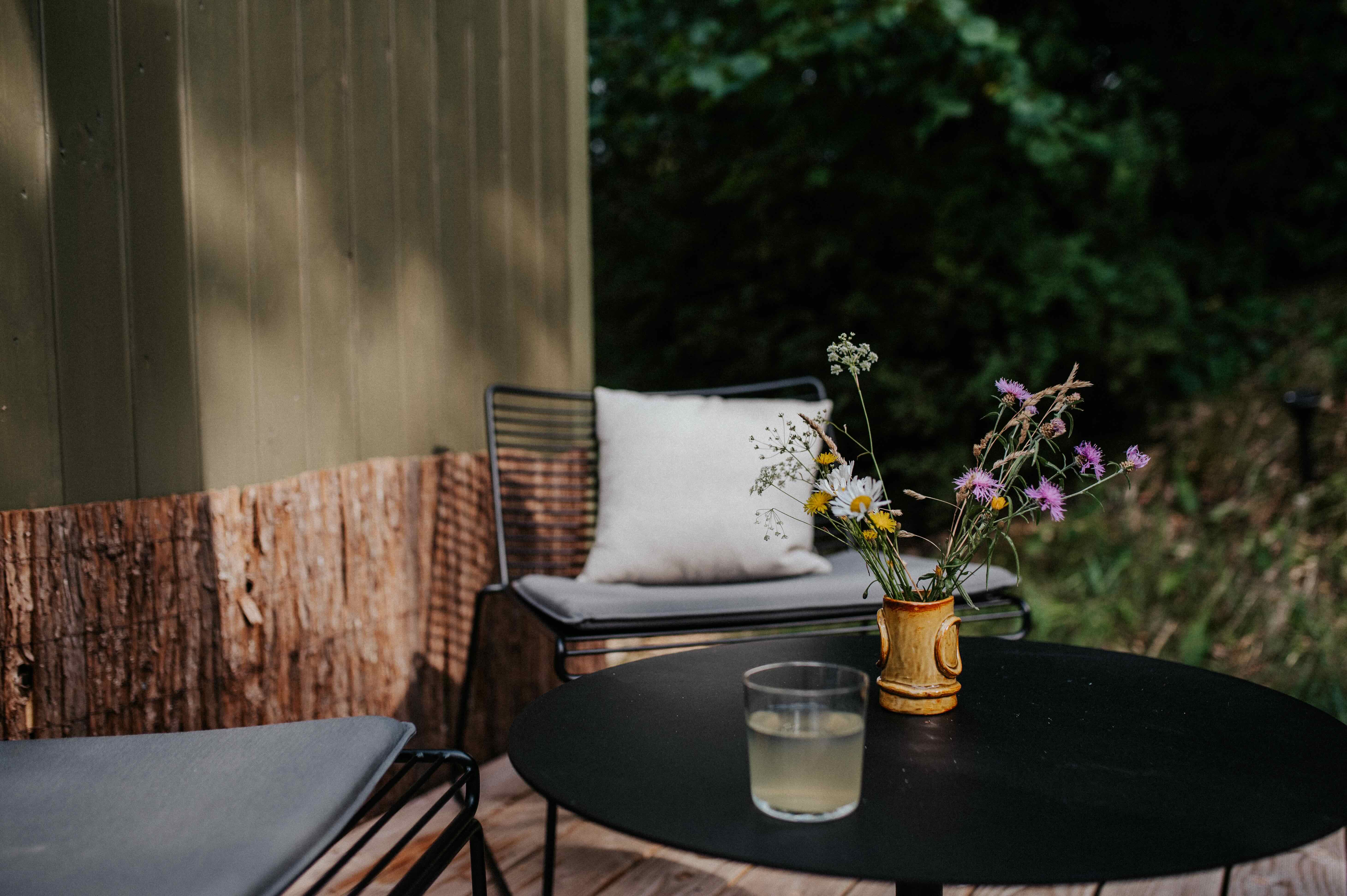 Zwei Stühle und ein Tisch mit Wiesenblumen auf der Terrasse einer Cabin am Waldrand