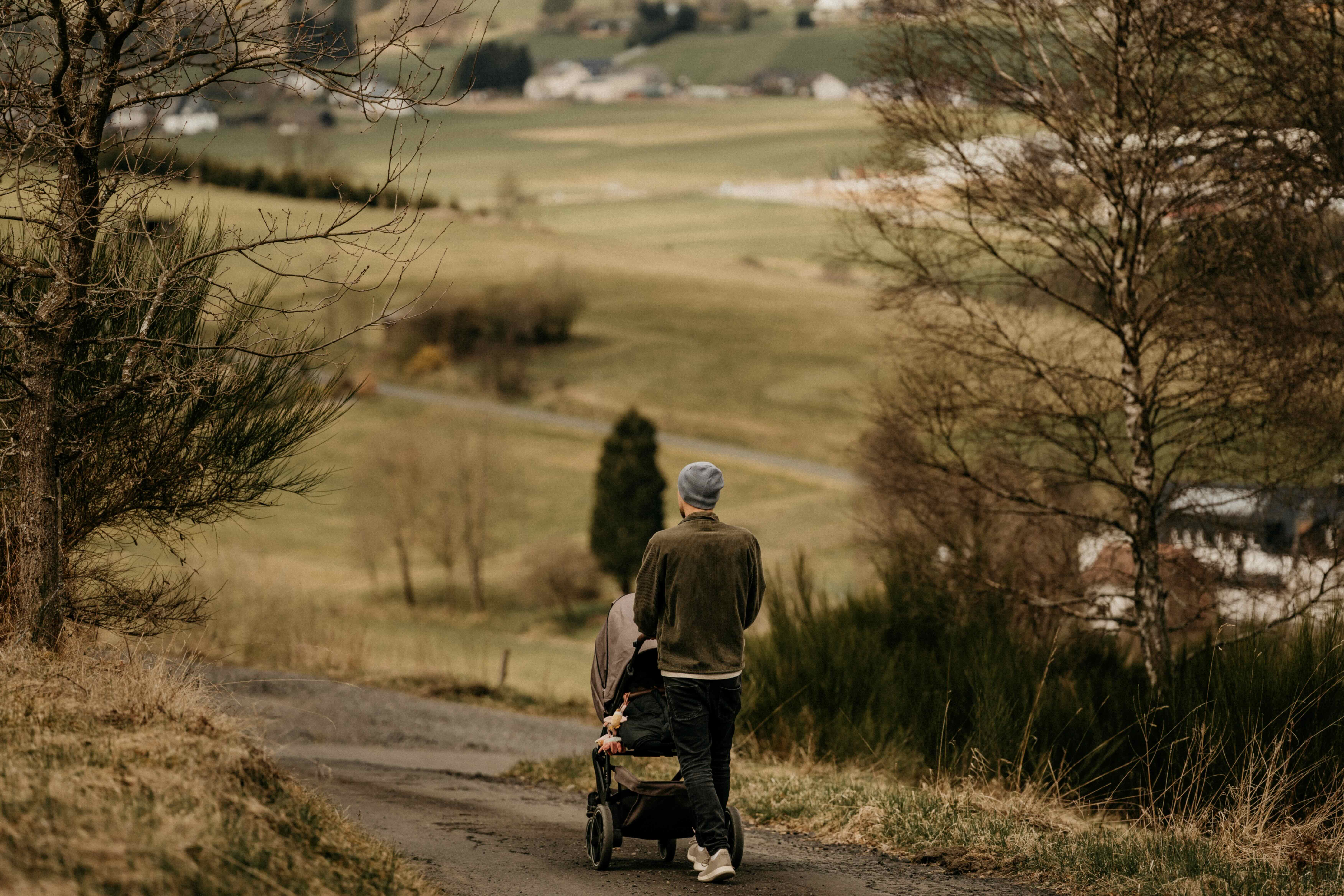 Vater schiebt einen Kinderwagen auf einem Feldweg über hügelige Wiesen