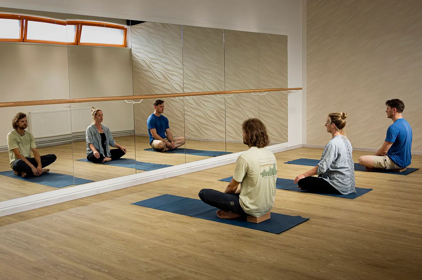 Eine Gruppe von drei Personen sitzt meditierend vor einem Spiegel im Yoga-Raum des Kraftwerk Althofens. 