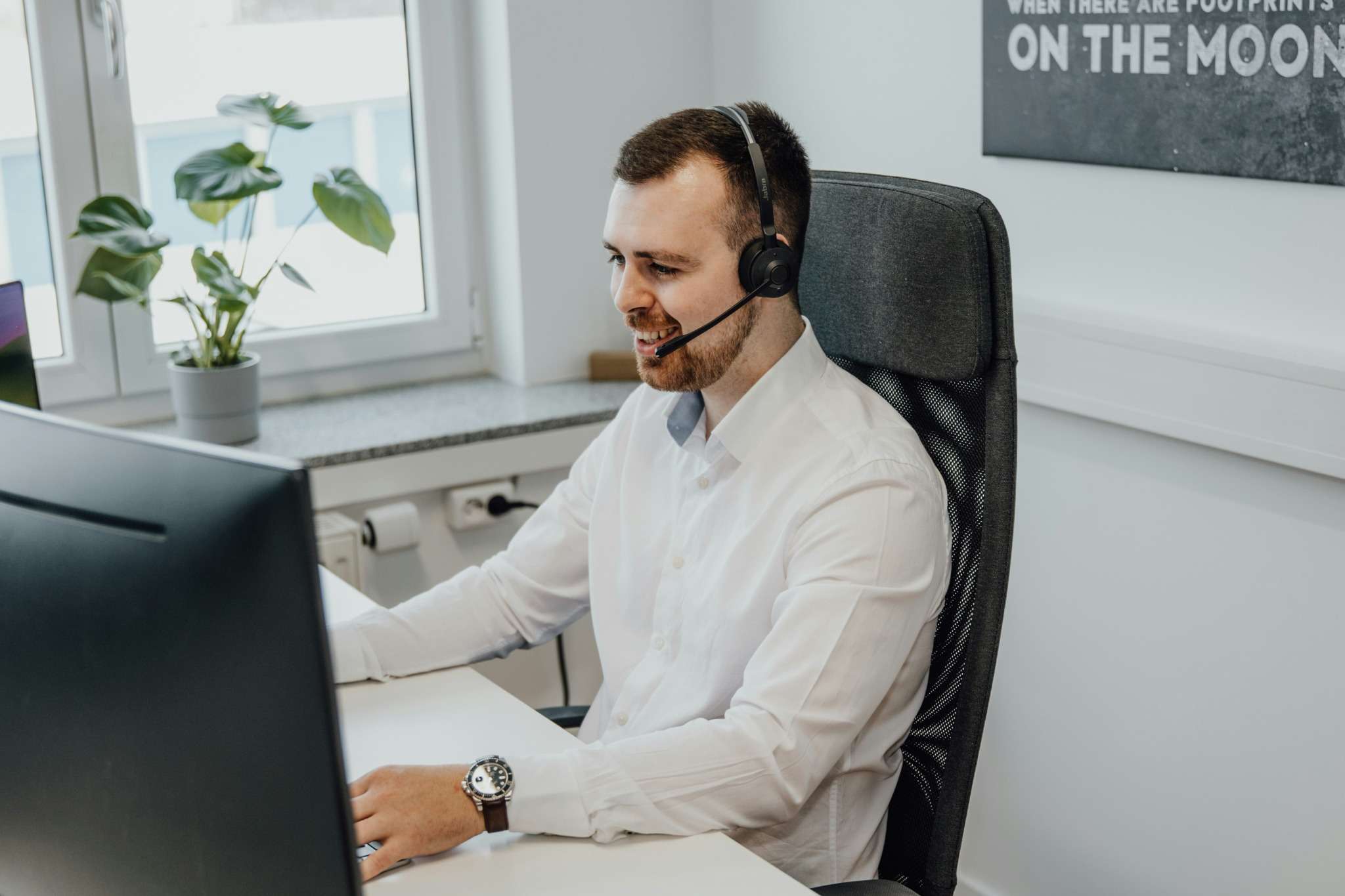 Un téléprospecteur souriant échange avec un client depuis son bureau.