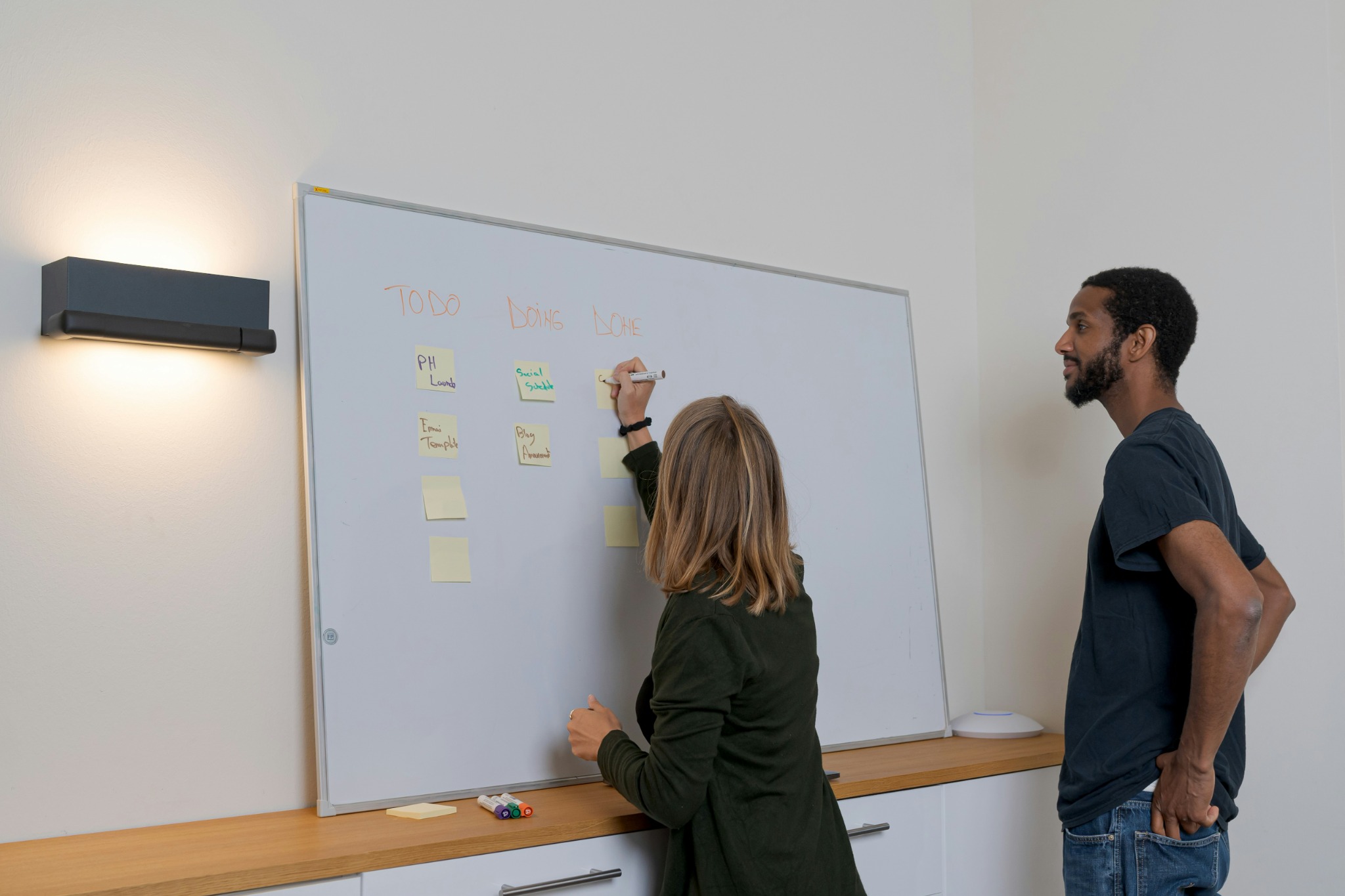 Une femme écrit sur un tableau blanc pendant qu’un homme observe.