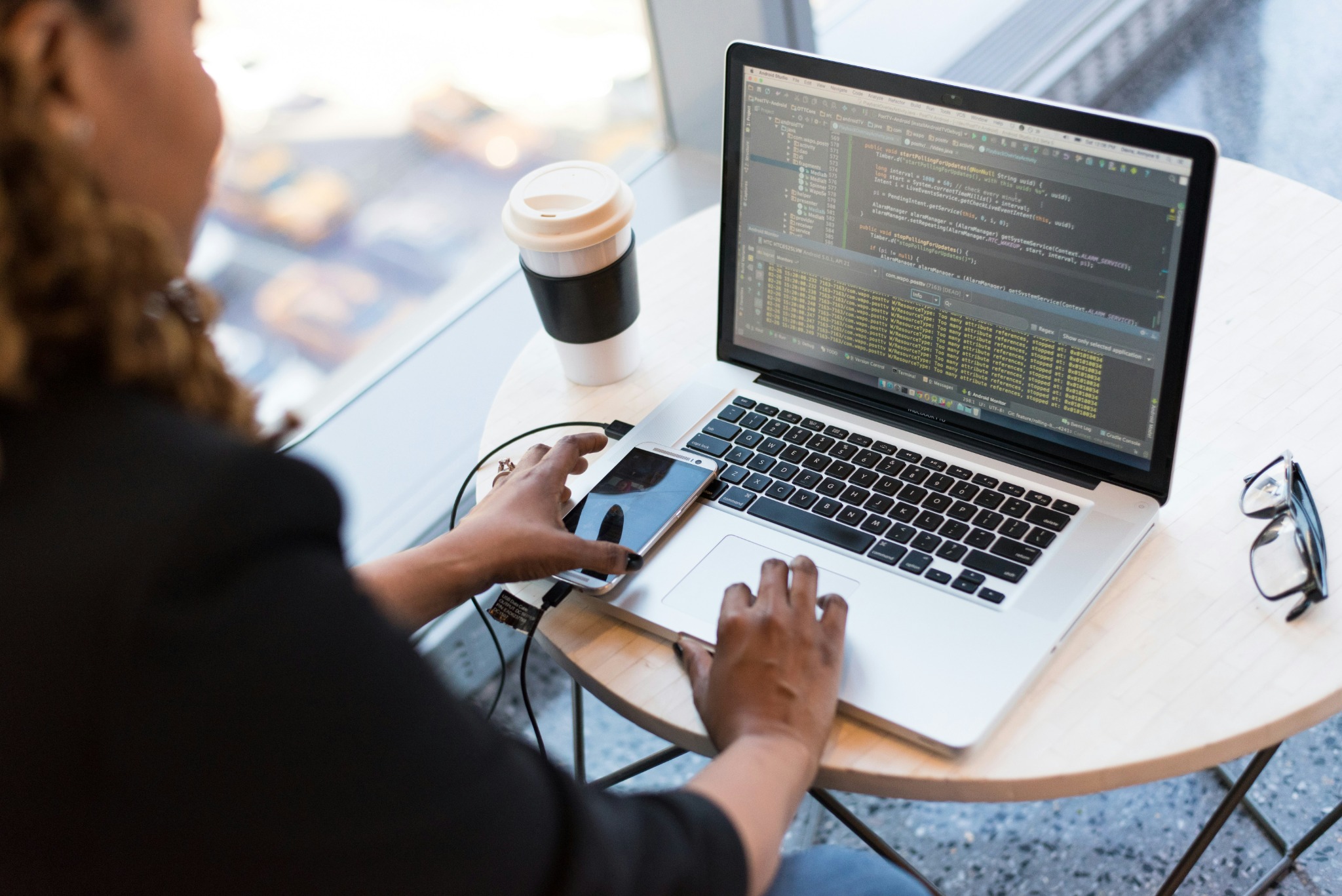 Une professionnelle code sur son ordinateur portable tout en utilisant son smartphone et un café à proximité.