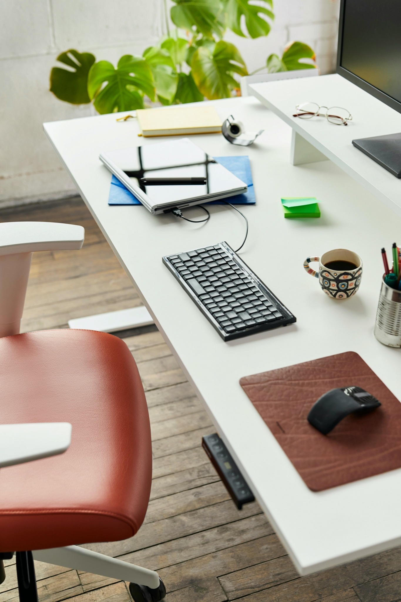 Un poste de travail moderne avec clavier externe, carnet, tasse de café et chaise ergonomique.