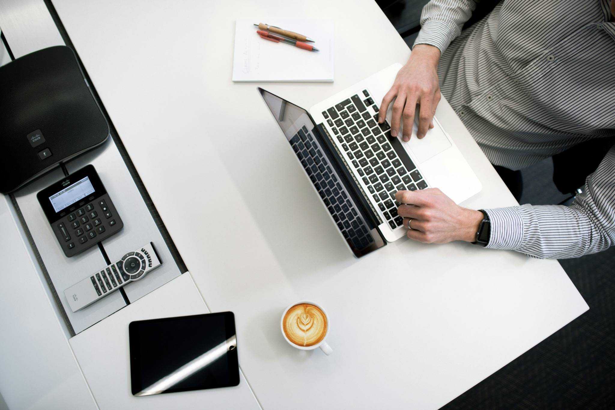 Travail en entreprise – Un professionnel travaille sur un ordinateur portable avec téléphone, tablette et café à portée de main.