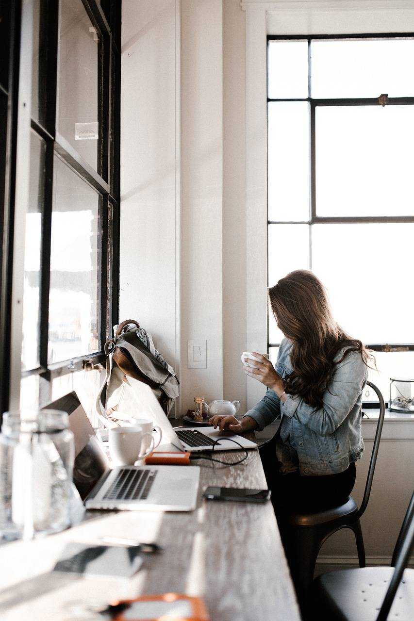 Une professionnelle utilise son ordinateur dans un espace lumineux, tout en prenant une tasse de café.