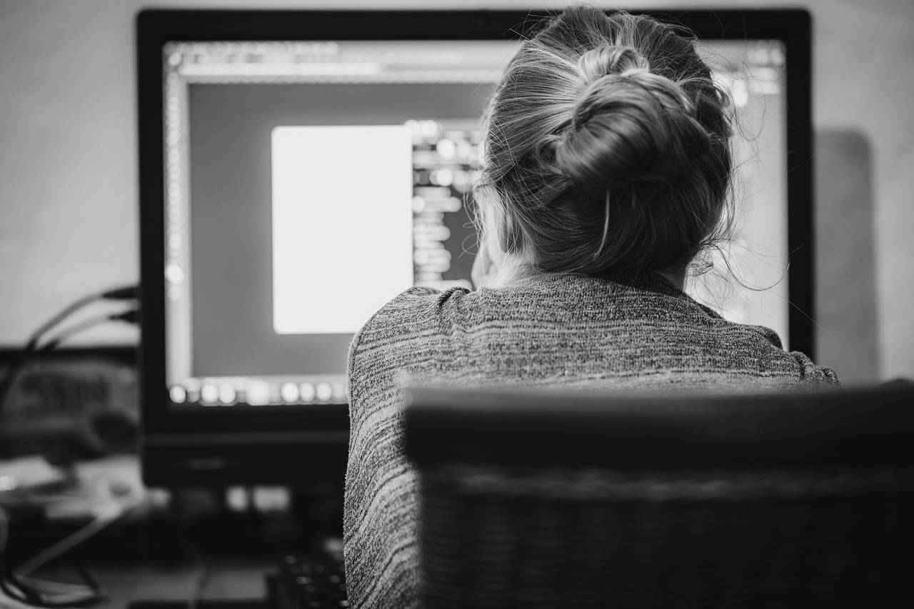 Une collaboratrice concentrée devant un grand écran d’ordinateur en noir et blanc.