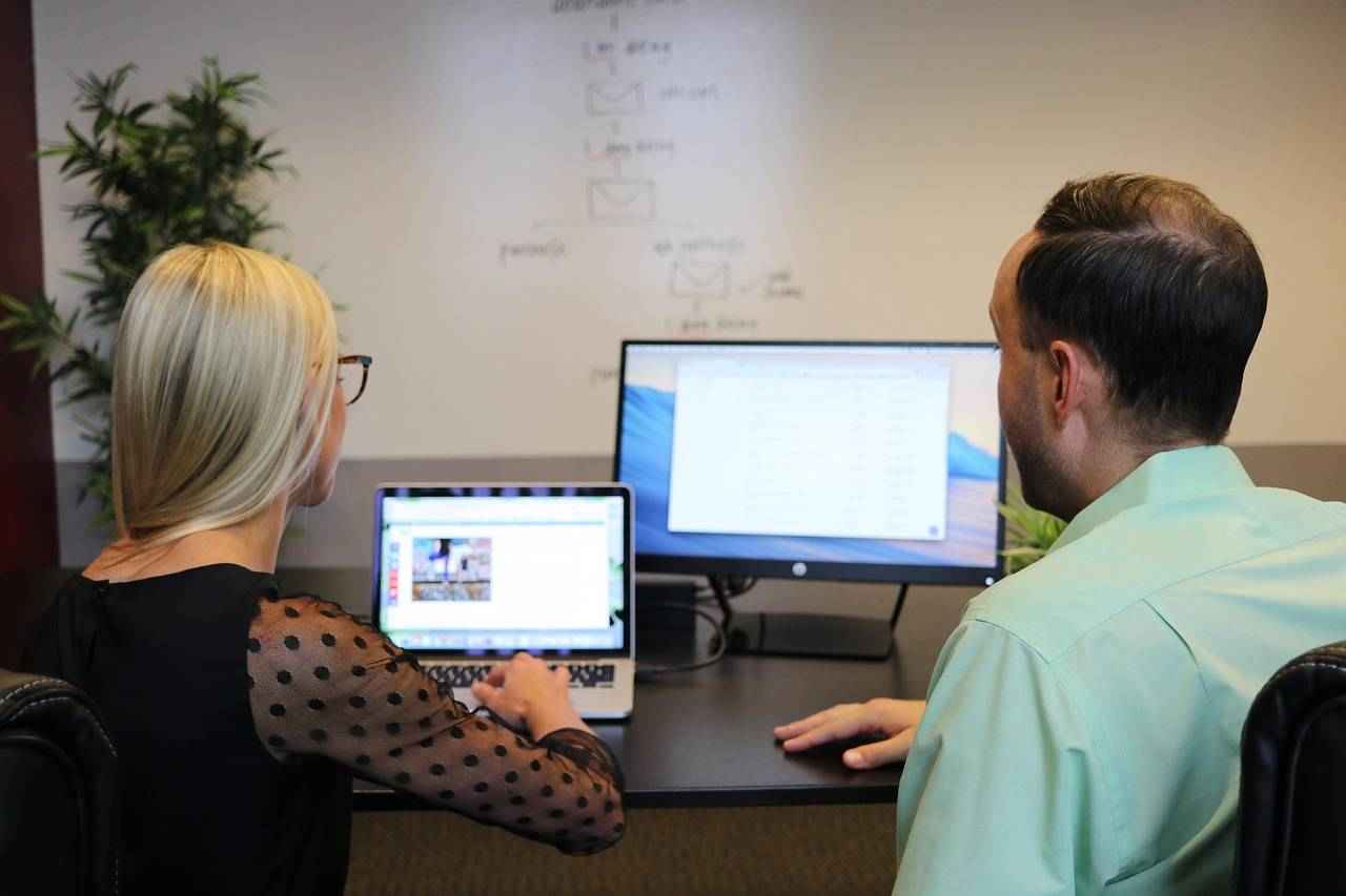 Deux collaborateurs analysent des données et échangent devant un ordinateur dans un cadre professionnel.