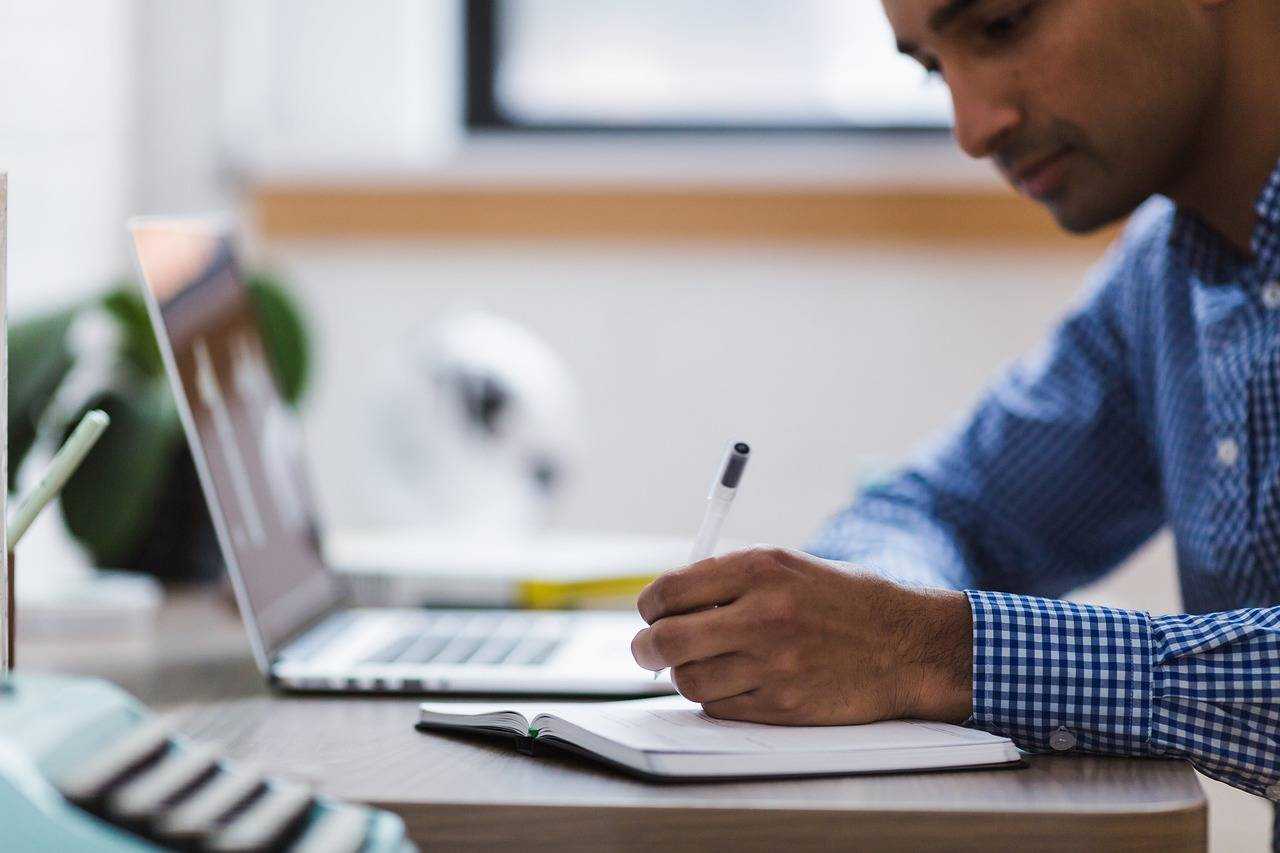 Un homme prend des notes devant son ordinateur portable, symbole d’apprentissage et de productivité
