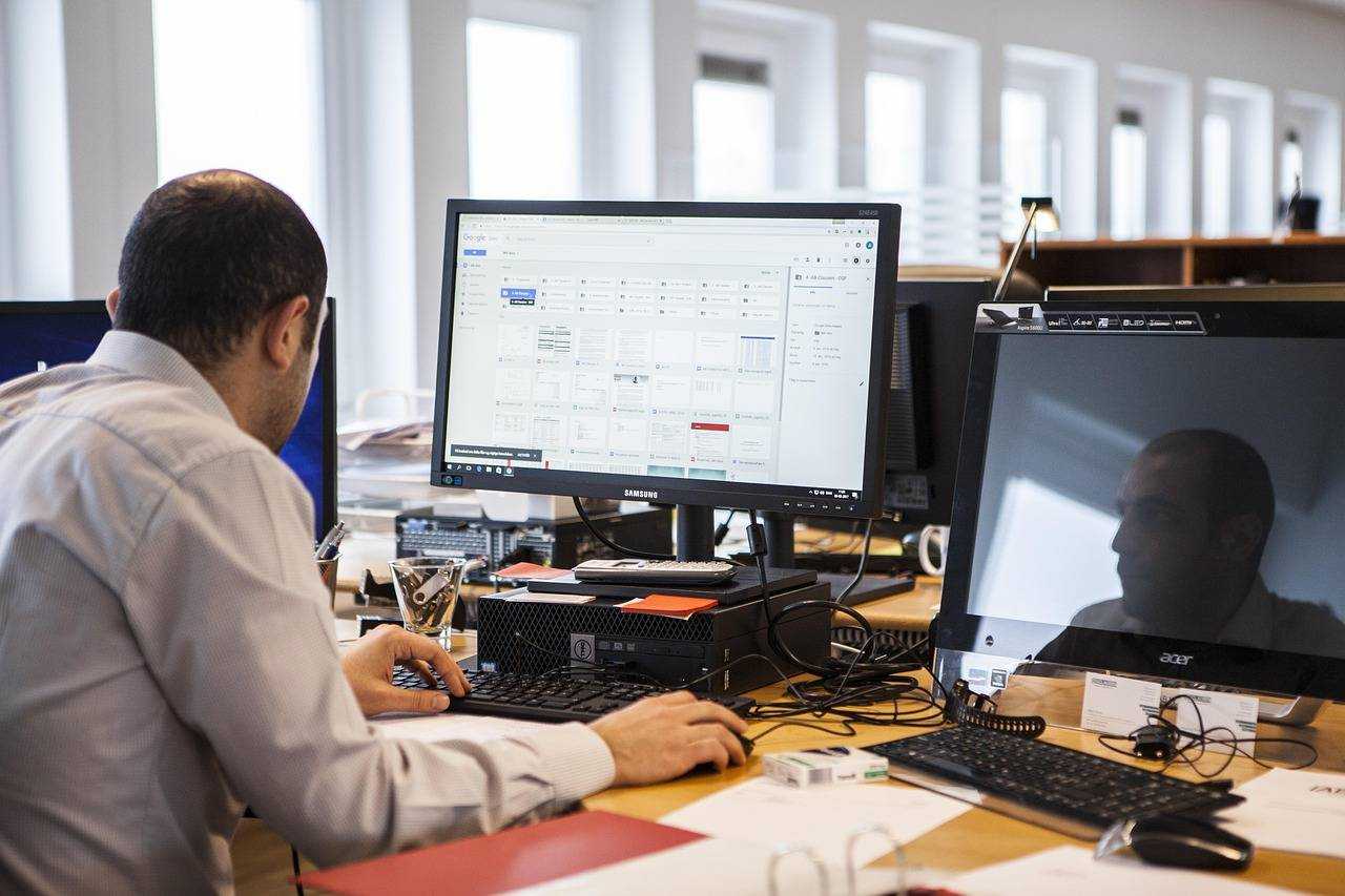 Employé concentré devant un double écran, travaillant sur des documents numériques dans un espace de bureau.