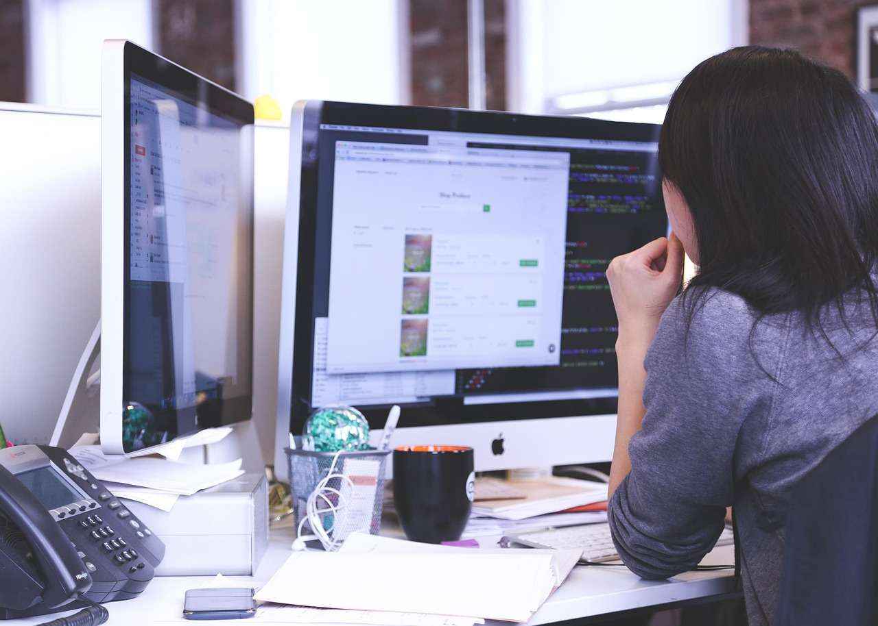 Professionnelle concentrée devant deux écrans d’ordinateur affichant des données et interfaces de travail.
