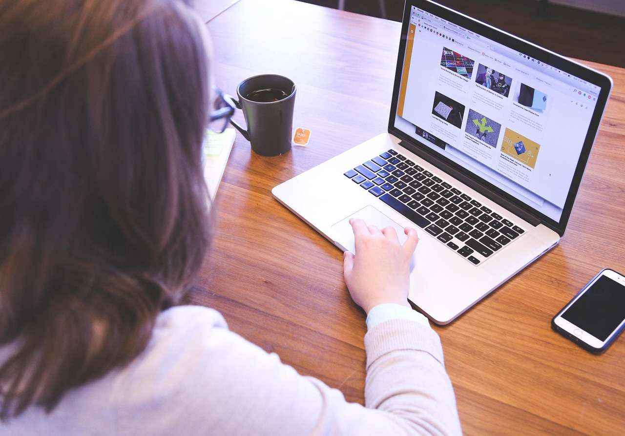 Utilisatrice consultant des pages web sur un ordinateur portable, accompagnée d’une tasse de thé et d’un smartphone.