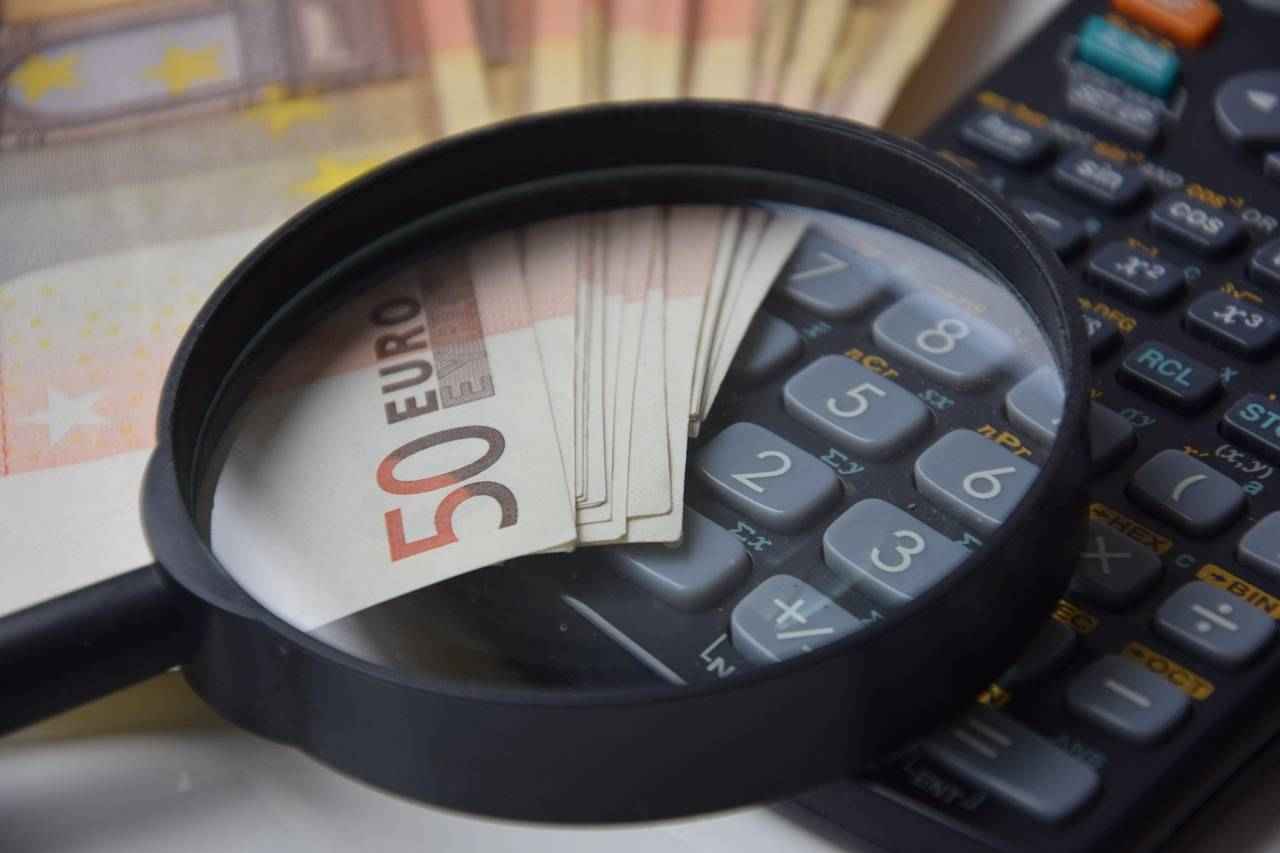 Des billets de 50 euros sous une loupe posés sur une calculatrice, symbolisant l’analyse des coûts et des finances.