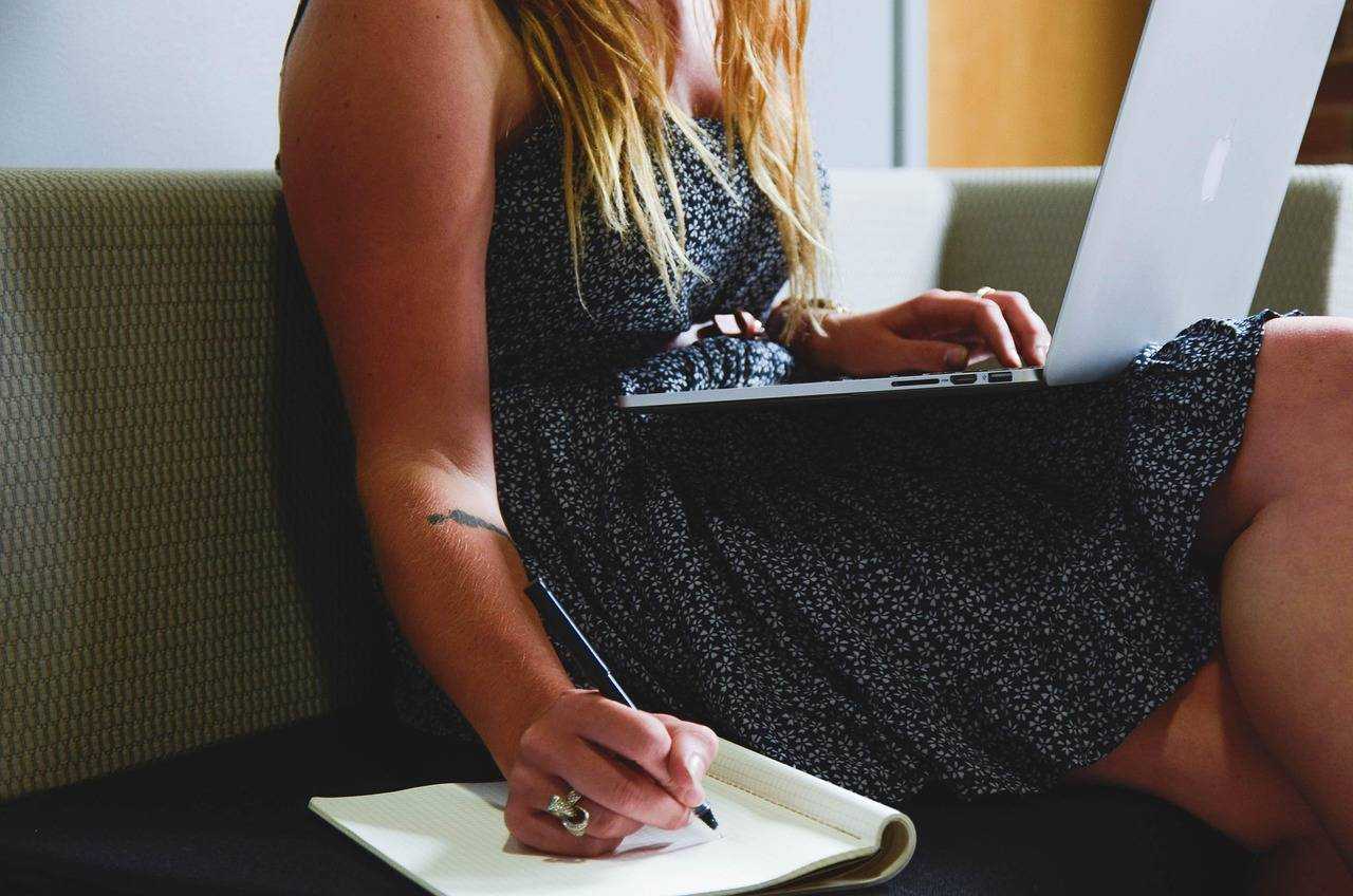 Une professionnelle prépare son script de prospection en prenant des notes tout en travaillant sur son ordinateur.