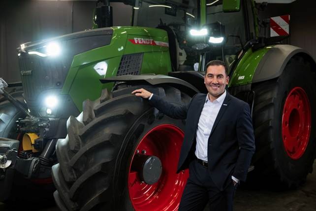 Dr Josef Mayer stands in a suit next to a large green tractor with red wheels.