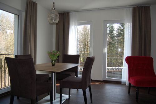 Helles Esszimmer im Waldhotel Rainau mit stilvollem Kronleuchter, großem Fensterblick ins Grüne und gemütlicher Sitzgruppe.