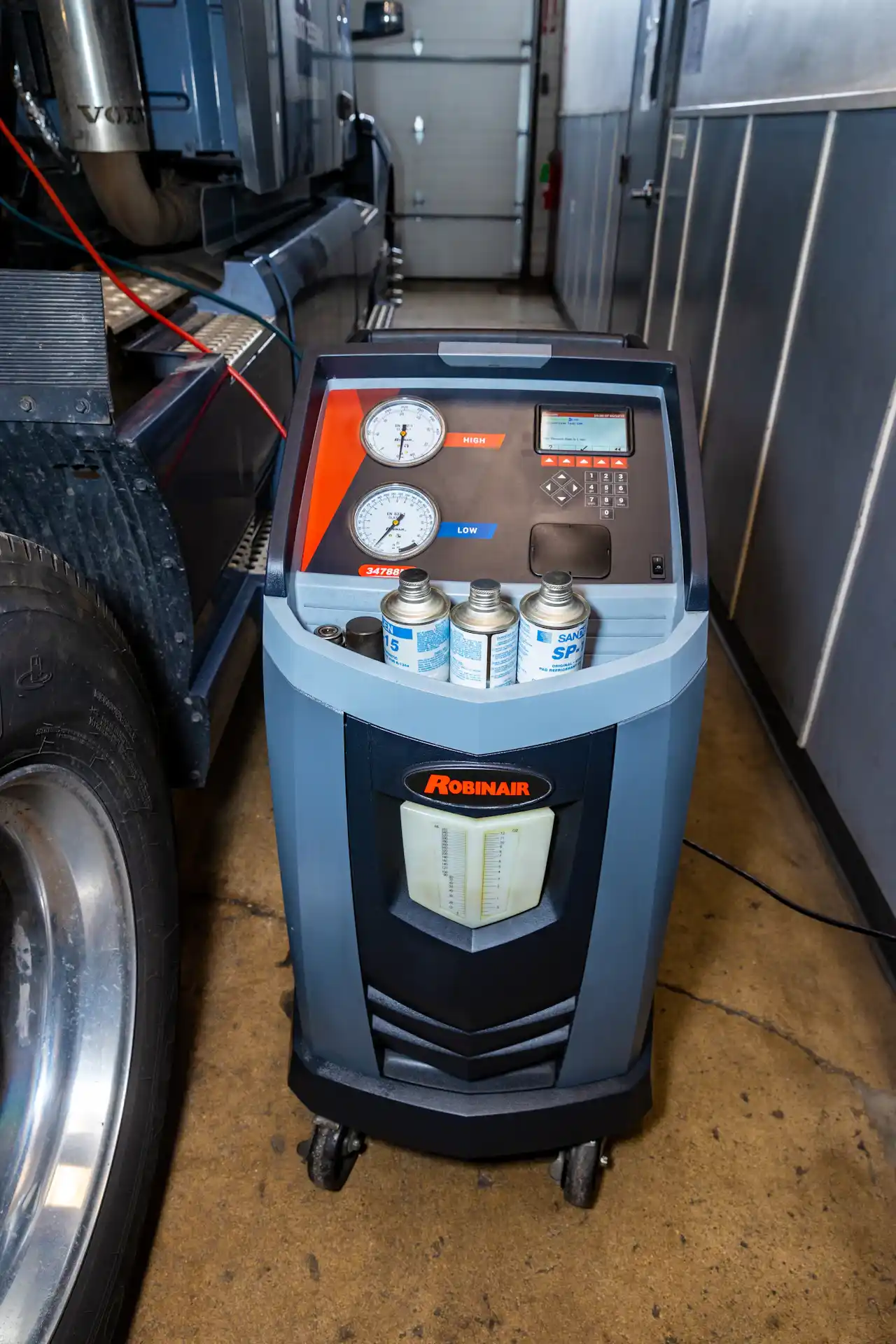 HVAC service using a Robinair A/C machine connected to a semi-truck for refrigerant recovery and system maintenance. The gauges are labeled "HIGH" and "LOW."