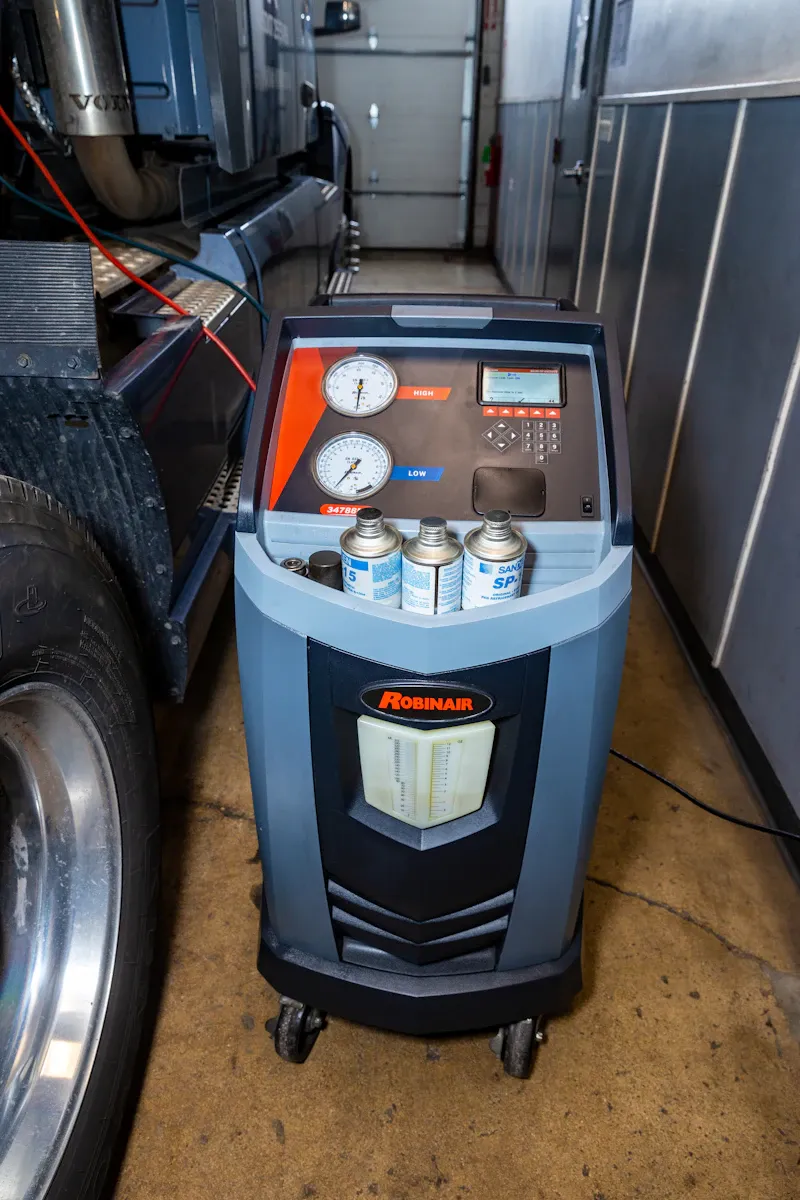 HVAC service using a Robinair A/C machine connected to a semi-truck for refrigerant recovery and system maintenance. The gauges are labeled "HIGH" and "LOW."