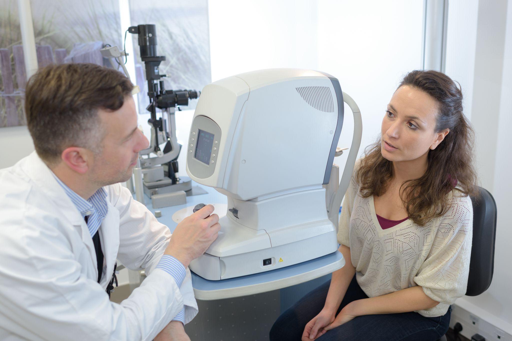 Doctor explaining eye exam procedure to patient sitting by advanced eye testing machine.
