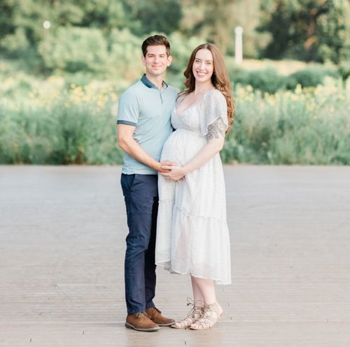 A joyful pregnant couple poses in front of a city field, symbolizing love and the excitement of welcoming a new life.