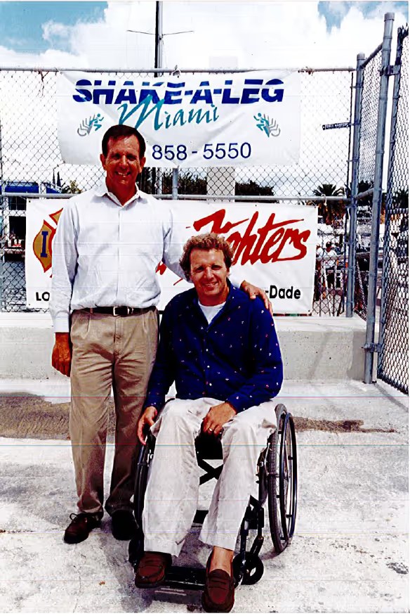 Harry Horgan in his wheelchair beside a colleague in front of the Shake-A-Leg Miami sign