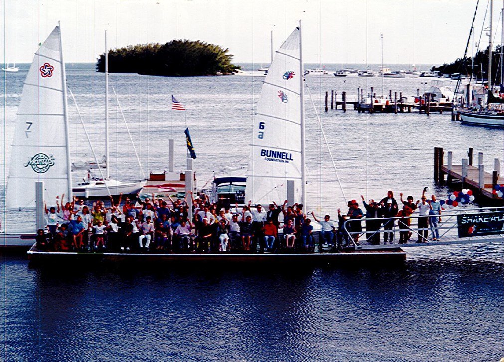 A pontoon boat crowded with participants alongside sailboats on Biscayne Bay
