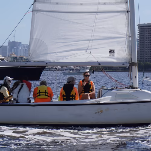 A keelboat crew in life jackets sailing past the Miami skyline