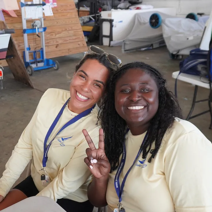 Two smiling Shake-A-Leg Miami volunteers in program T-shirts and lanyards, one making a peace sign