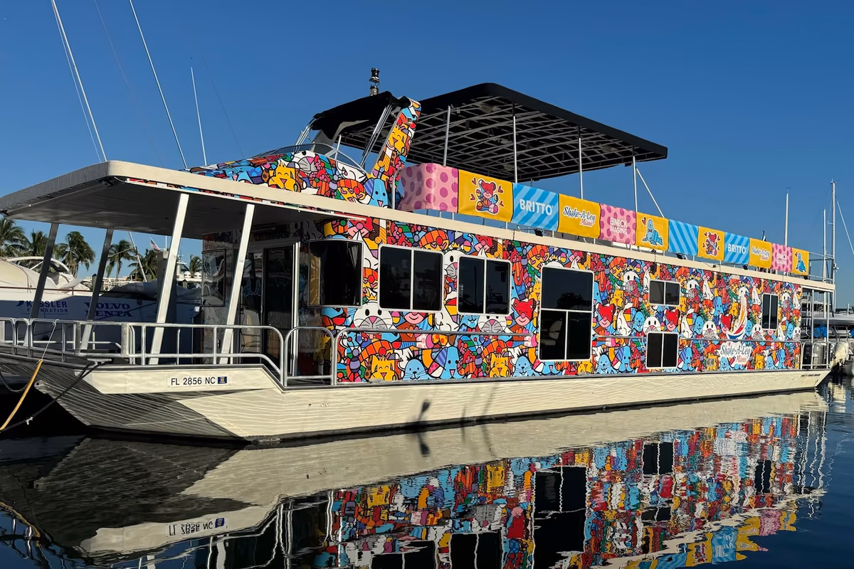 A houseboat covered in Romero Britto's bright hearts and patterns, reflected in the still water of the marina