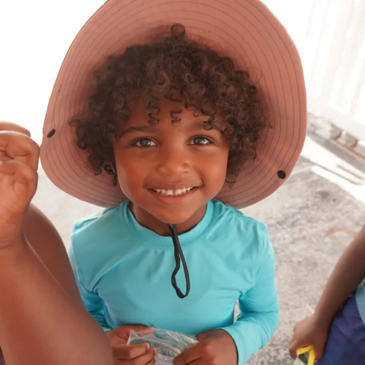 A young camper in a wide sun hat smiles at the camera