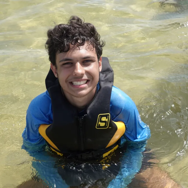 A smiling camper in a life jacket wades in the bay
