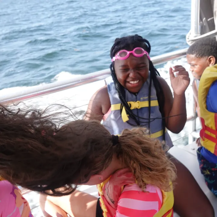 A camper in pink goggles laughs aboard a boat