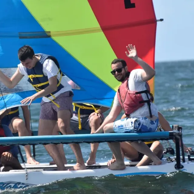 A crew in life vests sails a Hobie Cat with a rainbow sail on Biscayne Bay