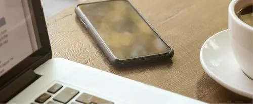 A laptop, a phone and a coffee cup at a table
