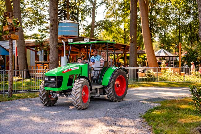 Eine Familie sitzt in einem Trecker und fährt durch einen Wald