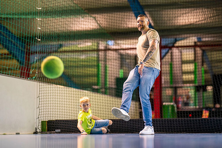 Ein Vater schießt einen Ball und sein Sohn schaut dabei zu