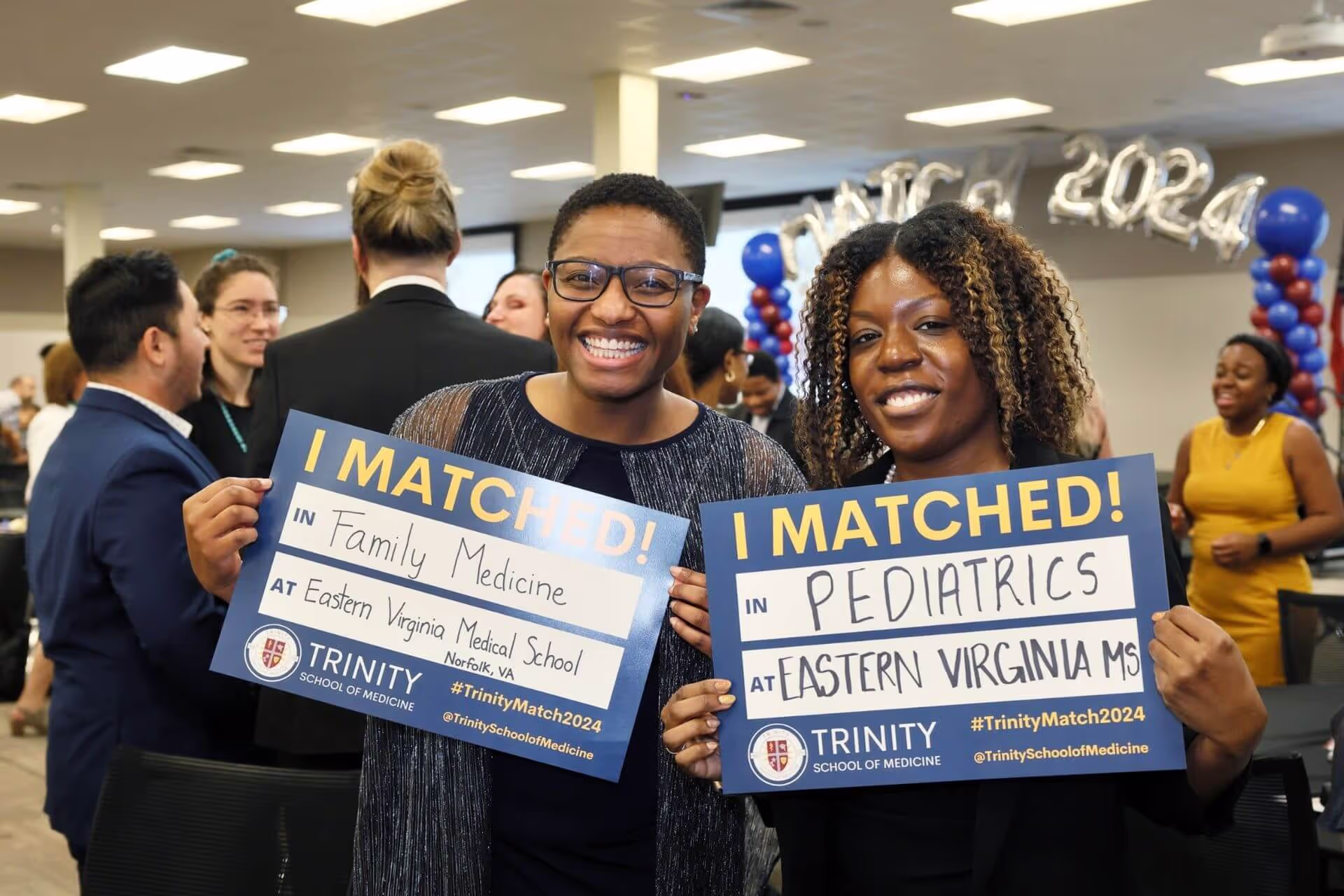 Two medical students at a matching ceremony holding signs showing they matched.