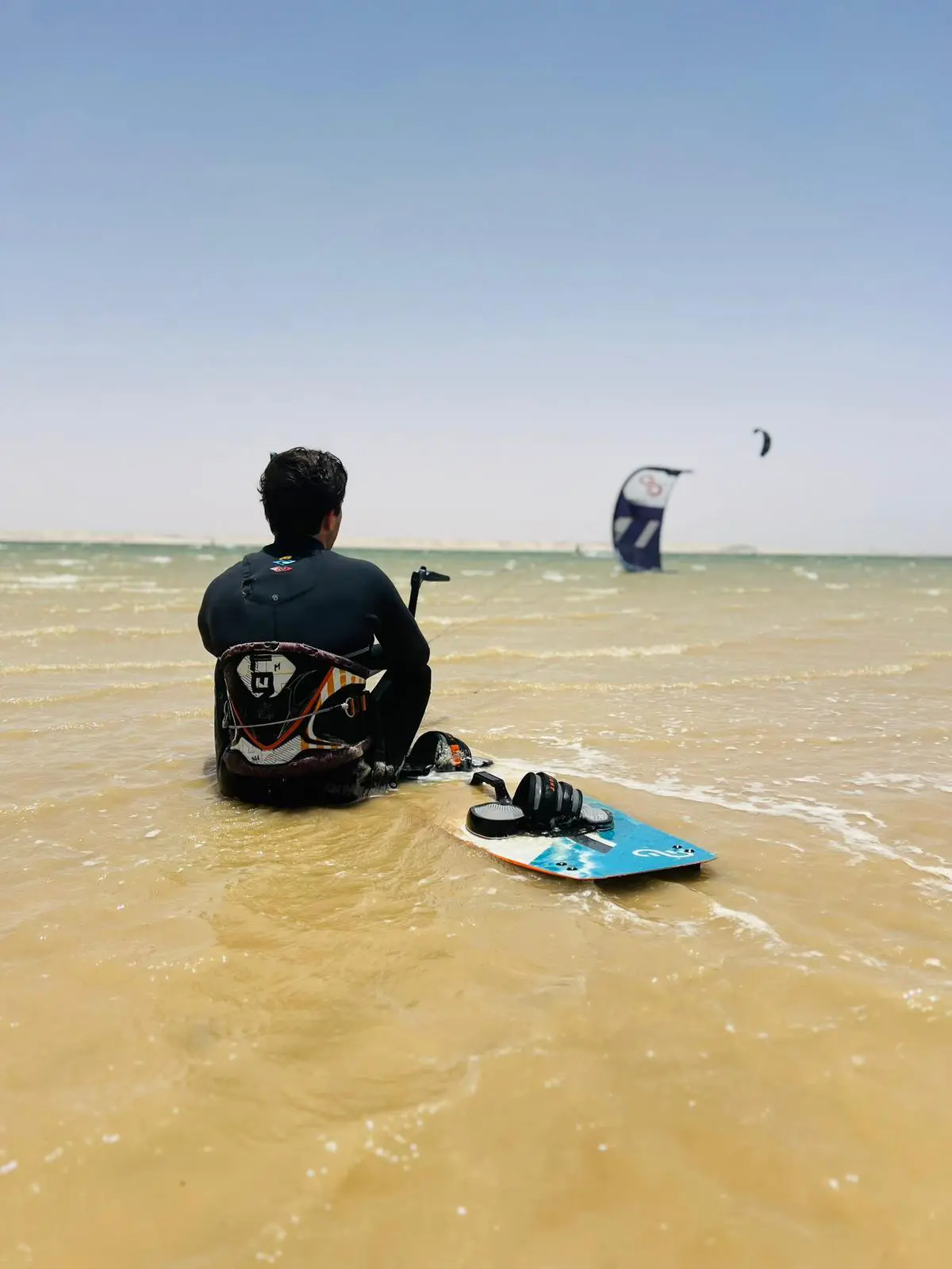 Kitesurfer sitting in shallow water with kiteboard at Dakhla Lagoon preparing for a session with Mirage Dakhla.