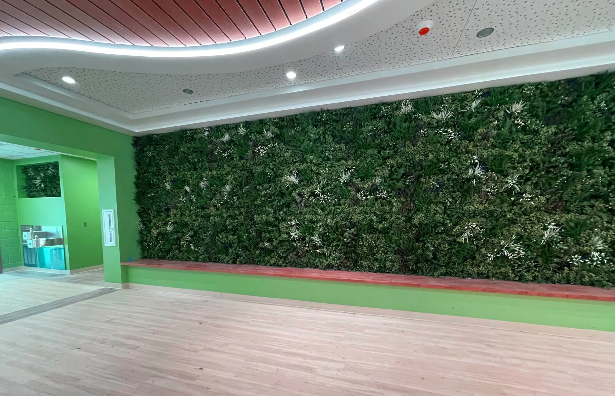 Long horizontal wall with full artificial plant covering from the seat to the ceiling.