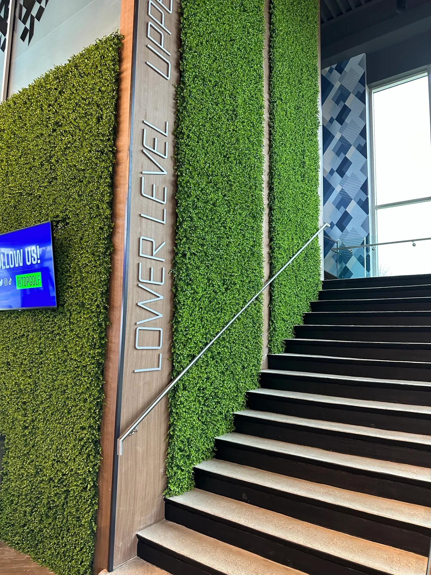 Interior of a commercial stairwell with a tall wall covered in artificial plants. 
