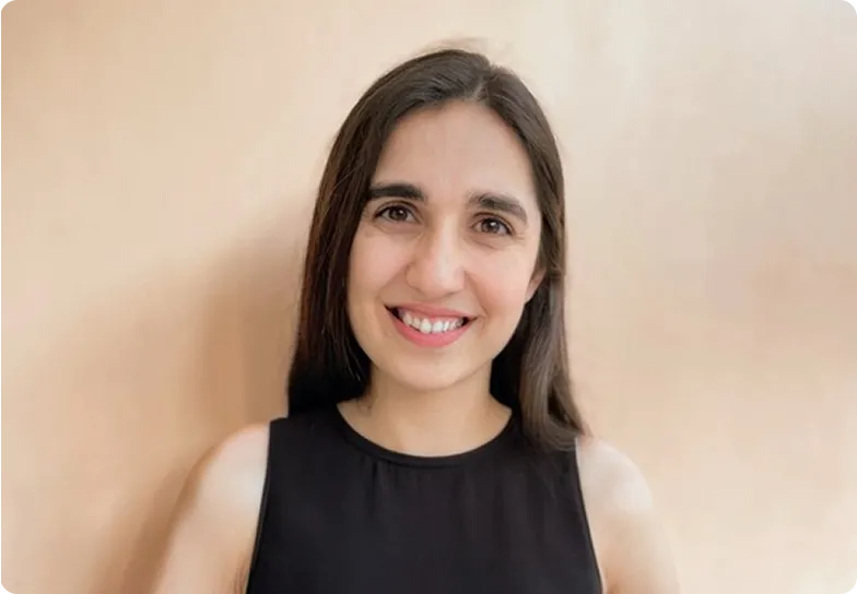 Smiling woman with long dark hair wearing a sleeveless black top against a beige background.