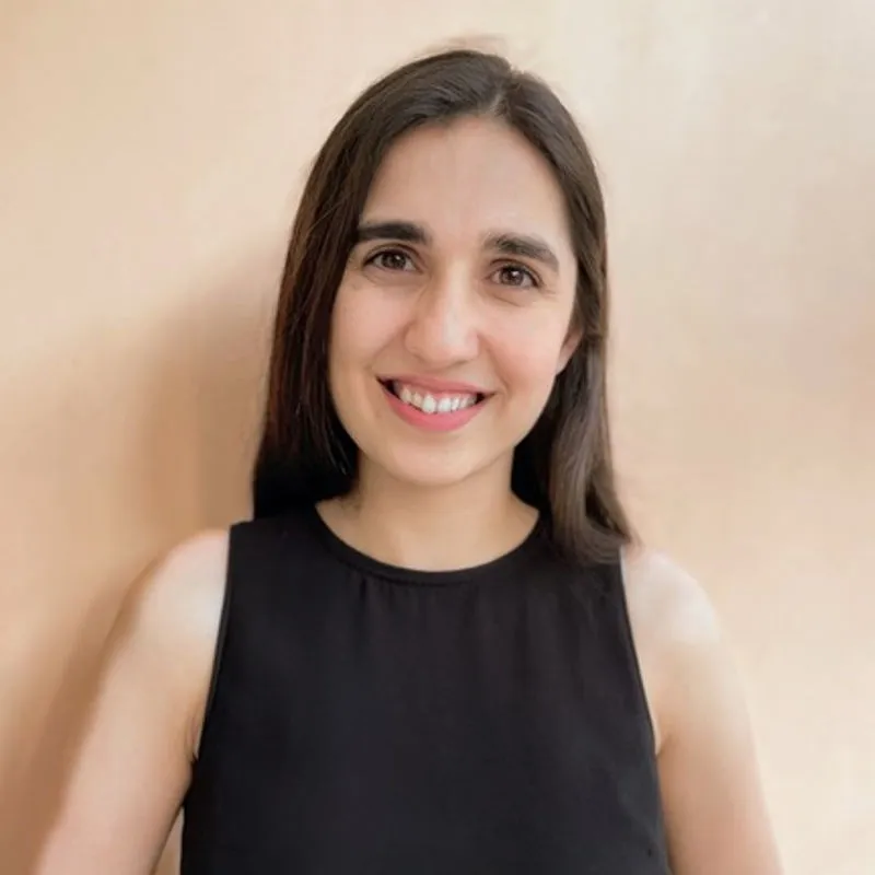 Smiling woman with long dark hair wearing a sleeveless black top against a beige background.