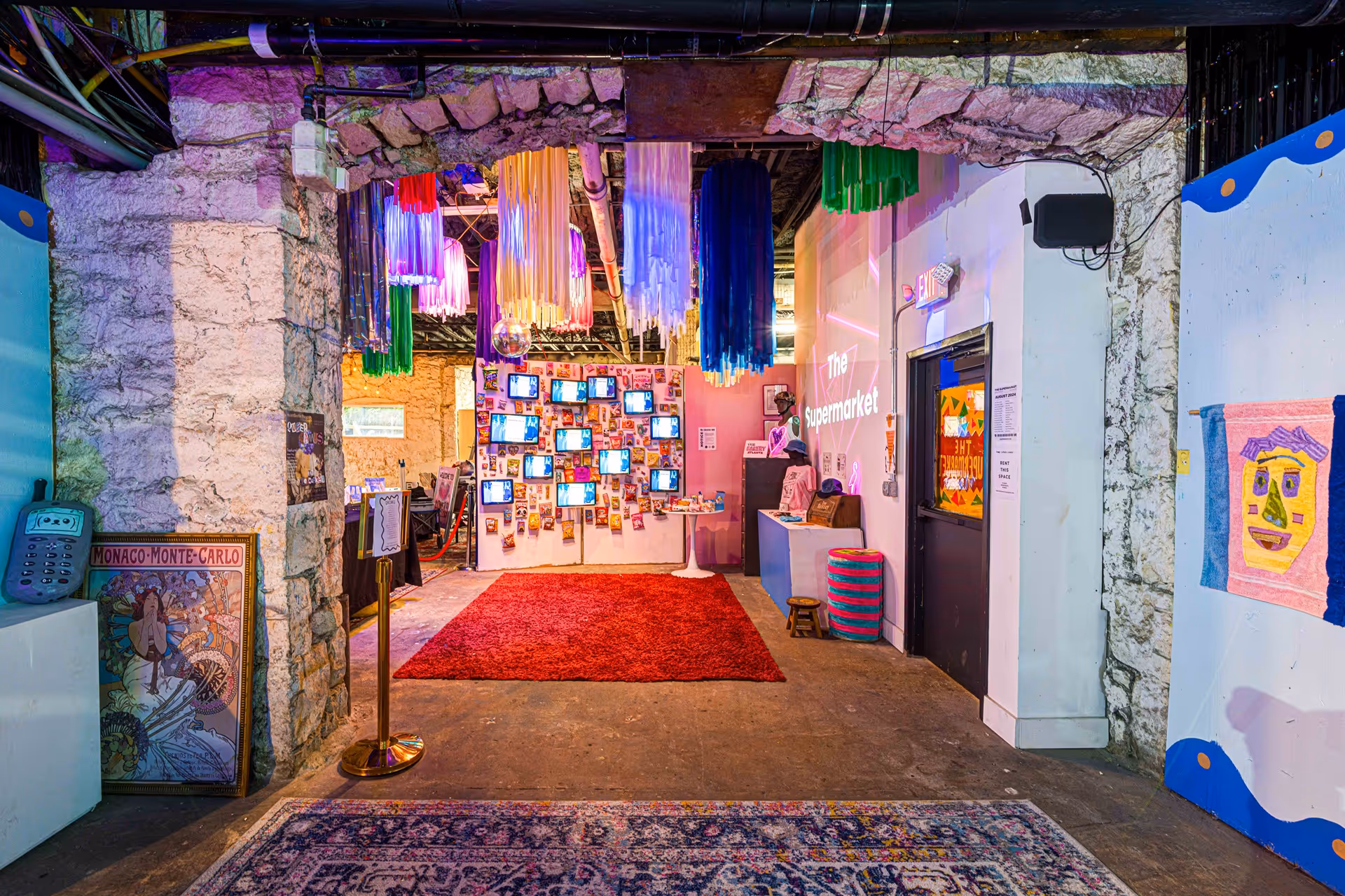 Entrance to The Supermarket Atlanta showcasing a vibrant and eclectic space with colorful hanging decorations, a wall of vintage televisions, and creative art installations, creating an inviting atmosphere for visitors.